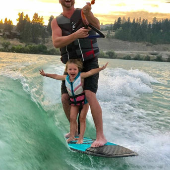 Man wake surfing with daughter on the board with him